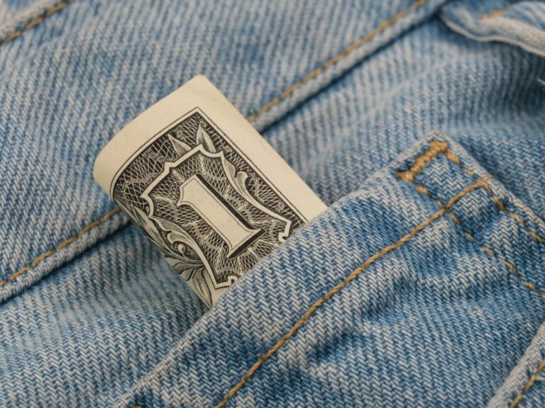 Close-up of a rolled dollar bill tucked into a denim pocket, symbolizing savings and finance.