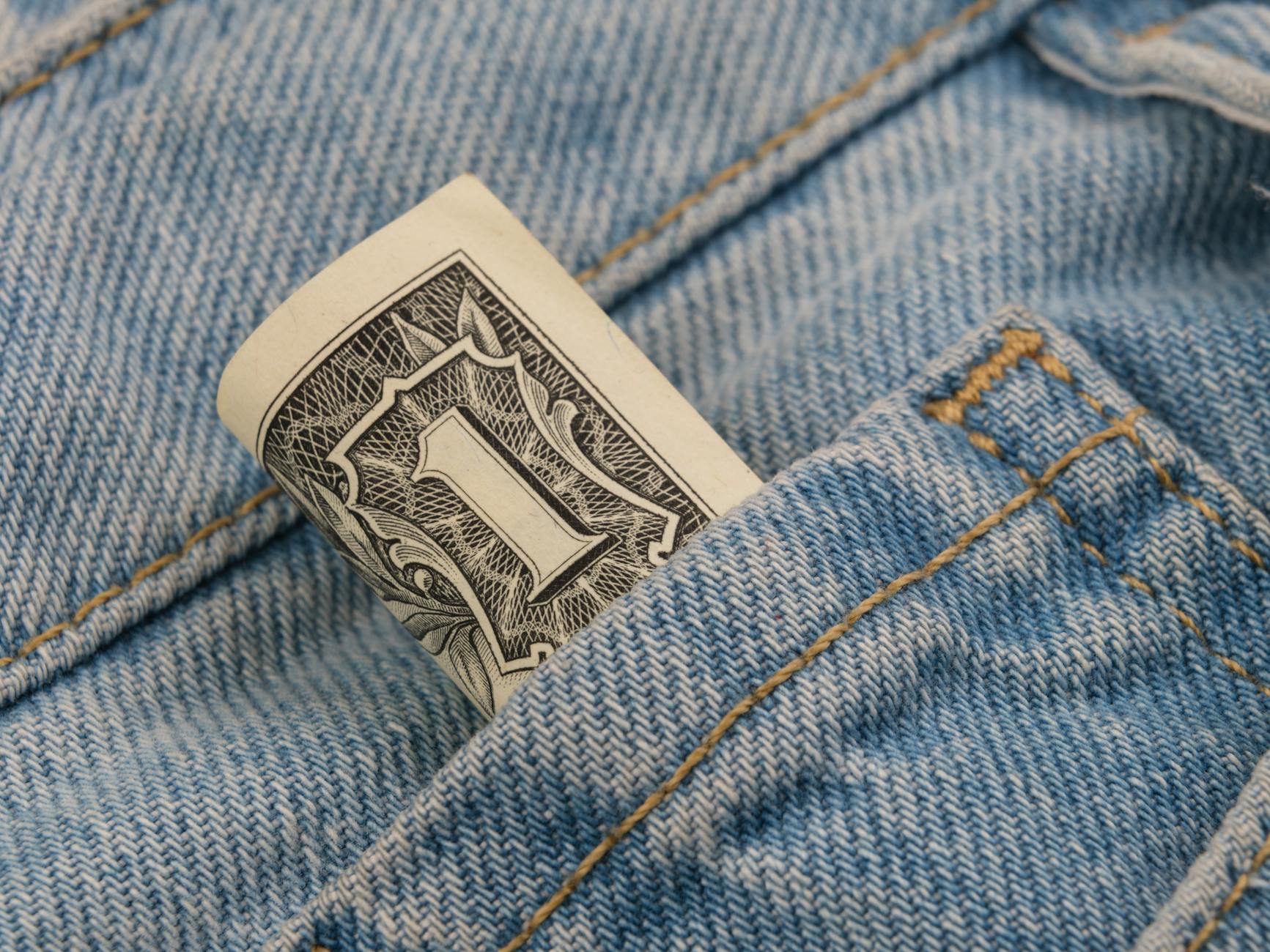 Close-up of a rolled dollar bill tucked into a denim pocket, symbolizing savings and finance.