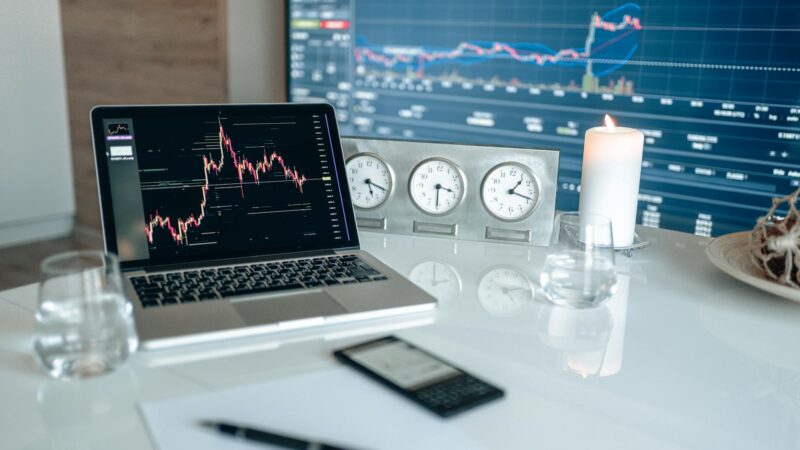 A modern workspace featuring financial charts and multiple clocks on a white table, ideal for trading.